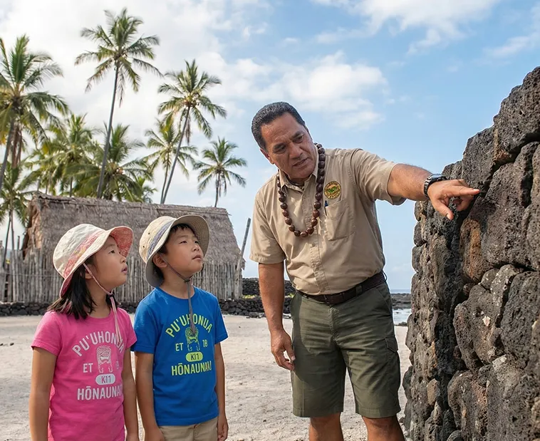 Man pointing out a stone wall to two children on a tropical beach
