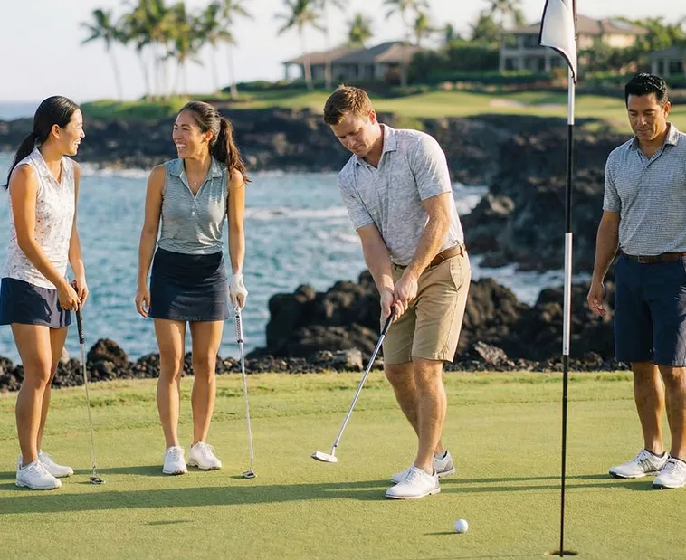 Four golfers standing on a green near the hole, with one preparing to putt