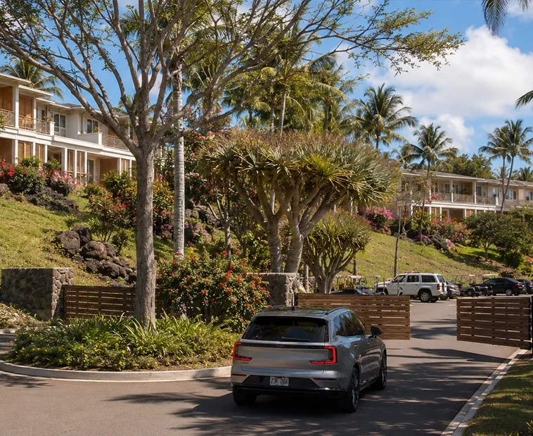 A car driving on a Hawaii townhome gated entrance road lined with palm trees and hillside buildings
